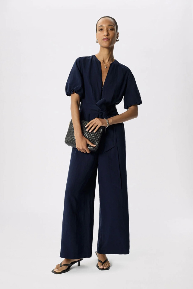 Model wearing black jumpsuit and holding a clutch